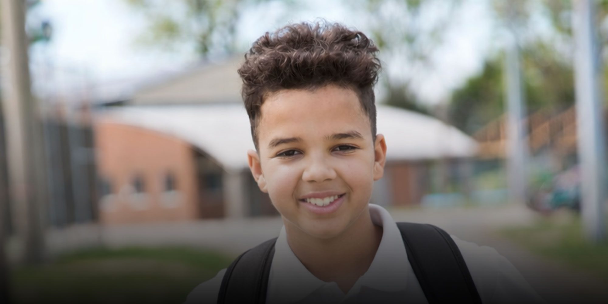 Smiling student with backpack standing outside of school
